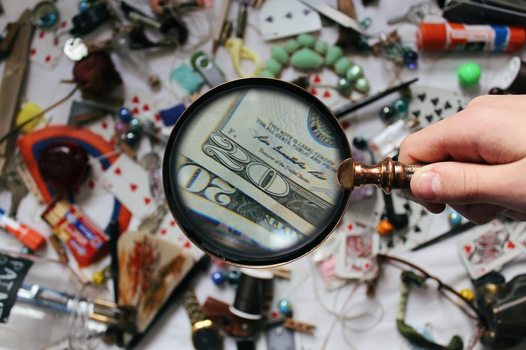Enhancing Your Understanding of Cerebratech: A Professional Research and Consulting Site A hand holding a magnifying glass focusing on a twenty dollar bill amidst various scattered objects.