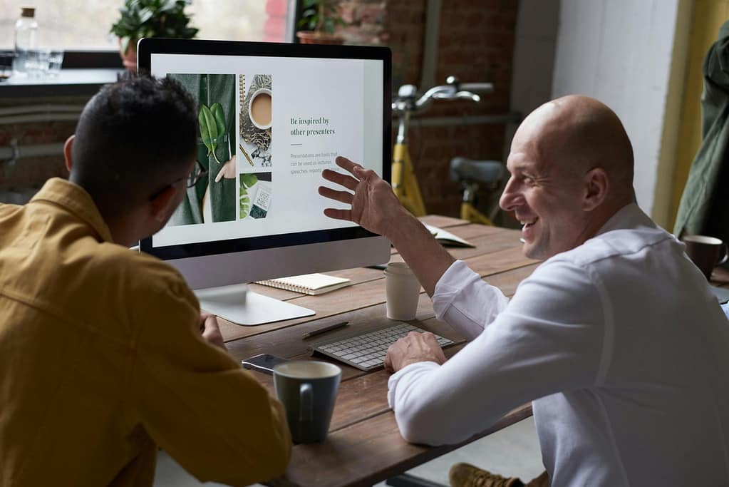 Blog Two professionals collaborating in a modern workspace, discussing a project on a computer screen.
