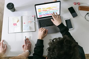 pexels photo 7213549 7213549 Two people collaborating on a laptop and planner at a vibrant modern office desk.